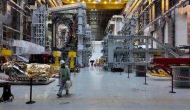 inside iter's tokamak assembly hall a high-cieling building filled with tokamak components and a worker walking by