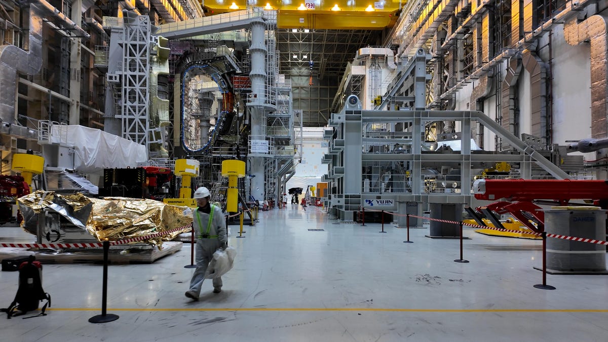 inside iter's tokamak assembly hall a high-cieling building filled with tokamak components and a worker walking by