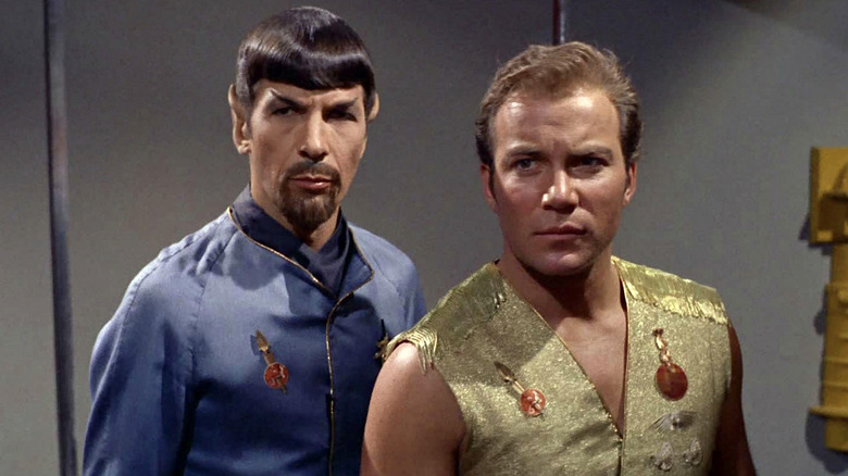 Spock in a blue shirt and Kirk in a gold vest standing next to each other in 