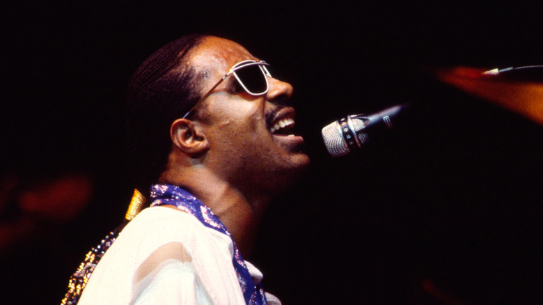 Stevie Wonder sat in sunglasses singing on stage