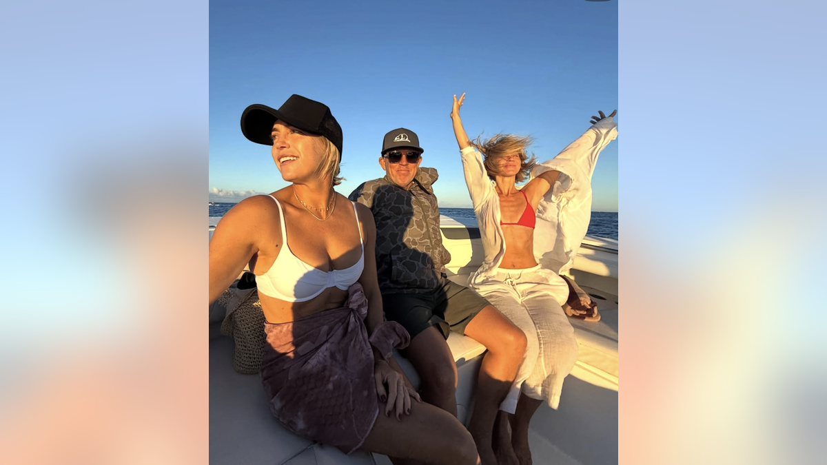 Julianne Hough with her arms in the air sitting on a boat with friends
