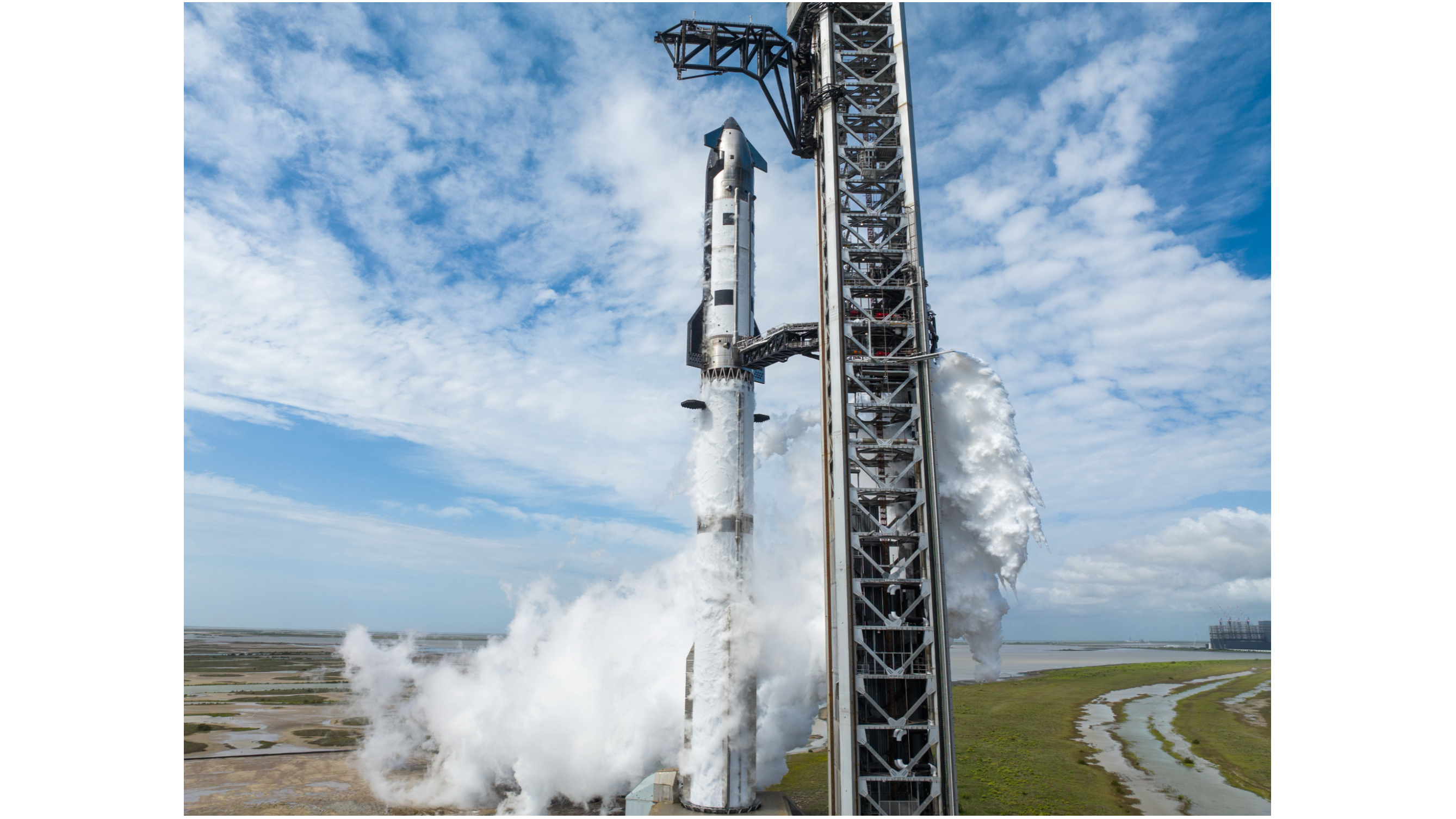a tall silver rocket stands on a launch pad beneath a blue sky strewn with clouds