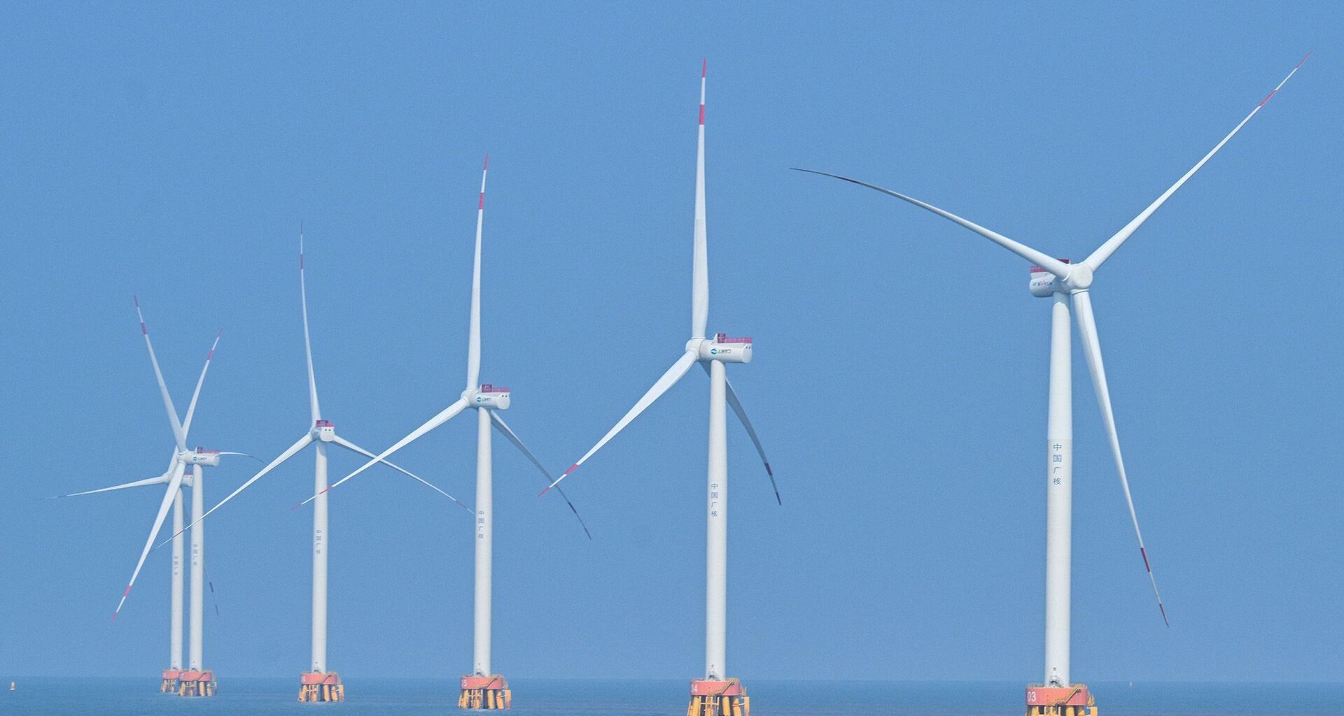A series of white wind turbines sit in the ocean.