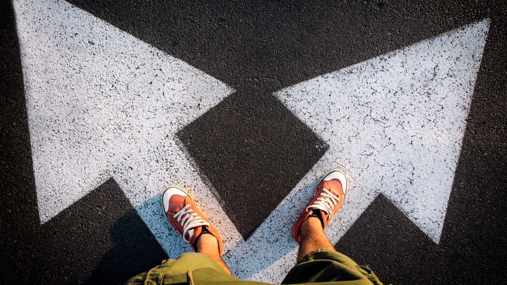 A person standing on a crossroad, with arrows pointing in different directions.