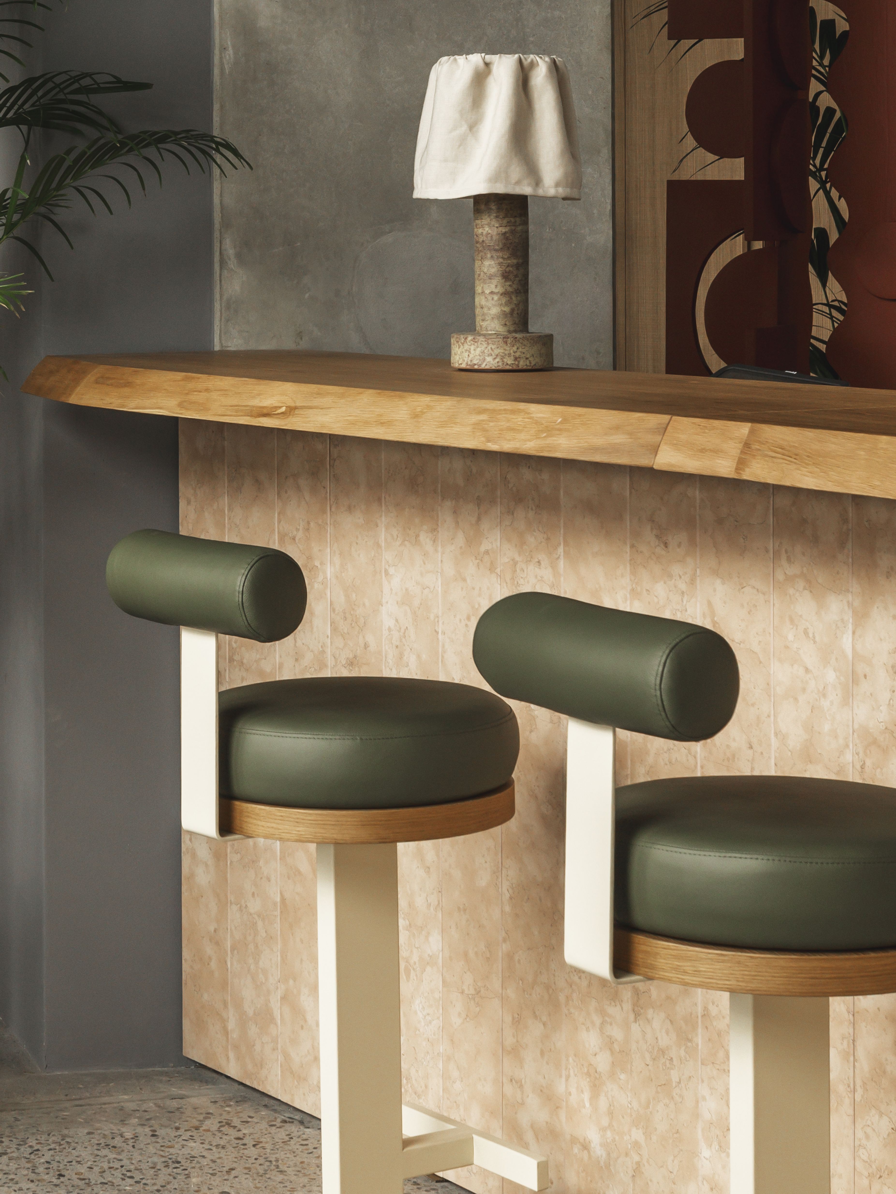 A brutalist shell of a hotel where cement walls and tall ceilings are softened by warm woods, textural fabrics, soft forms, and pendant lighting in earthy tones.