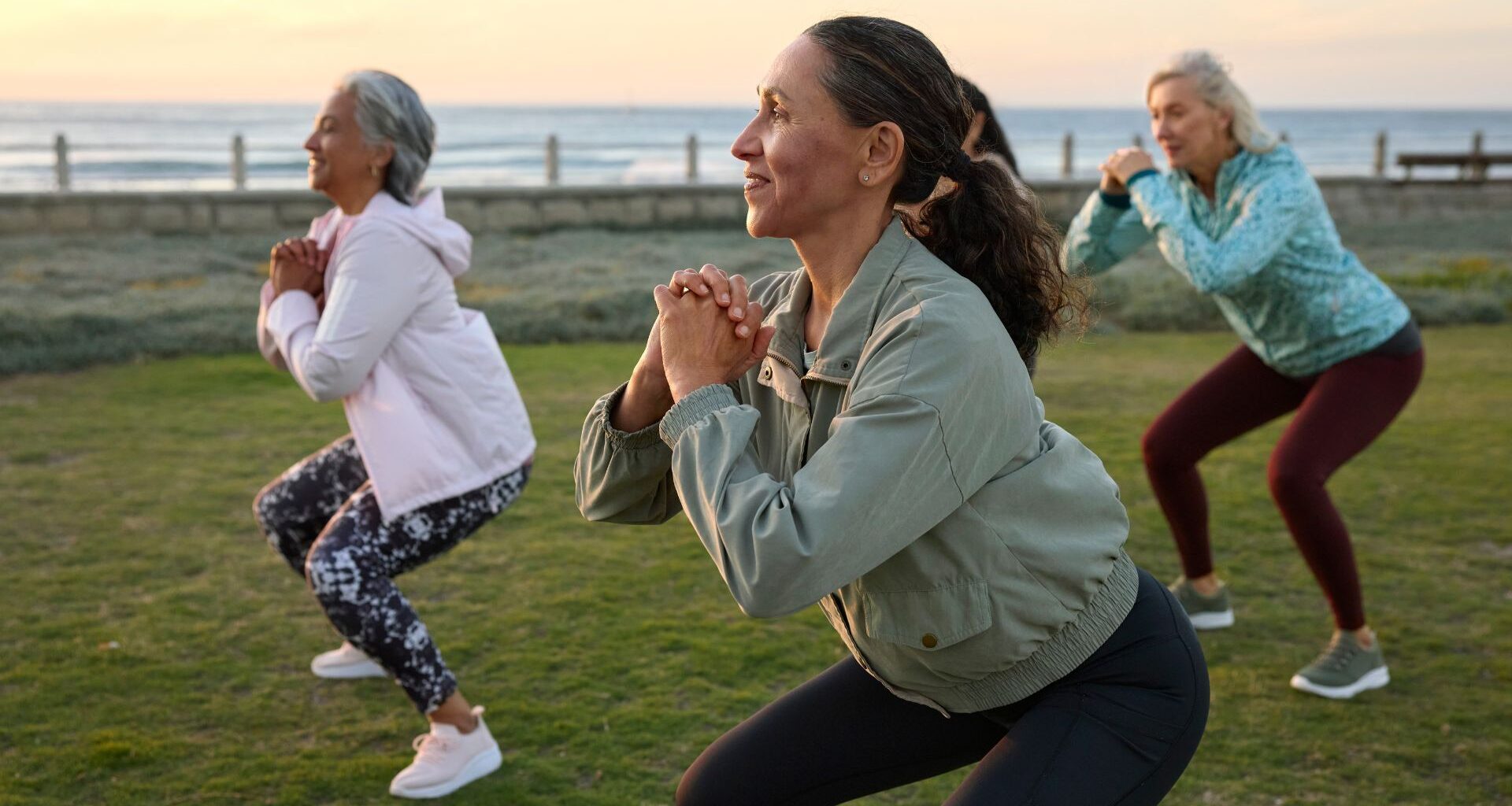 Women doing squats as part of yoga as strength training together outdoors in the summer by the sea