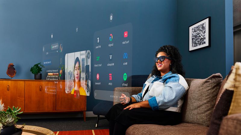 From iPhoneIslam.com, a person wearing augmented reality glasses sits on a sofa in a modern living room, interacting with virtual interfaces displayed in the air.