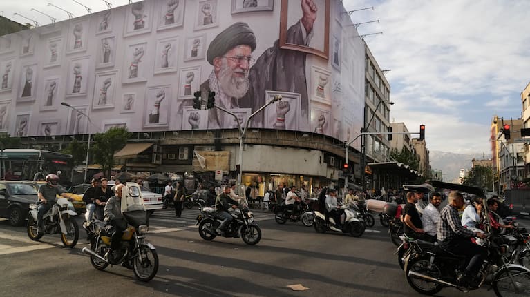 Motorbikes drive past a billboard with graphic showing the late Iranian Supreme Leader Ayatollah Ali Khamenei.