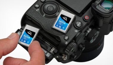 A hand inserts a memory card labeled “960GB” into a camera. Another memory card labeled “480GB” is inserted beside it. The camera shows detailed buttons and controls near the card slots.