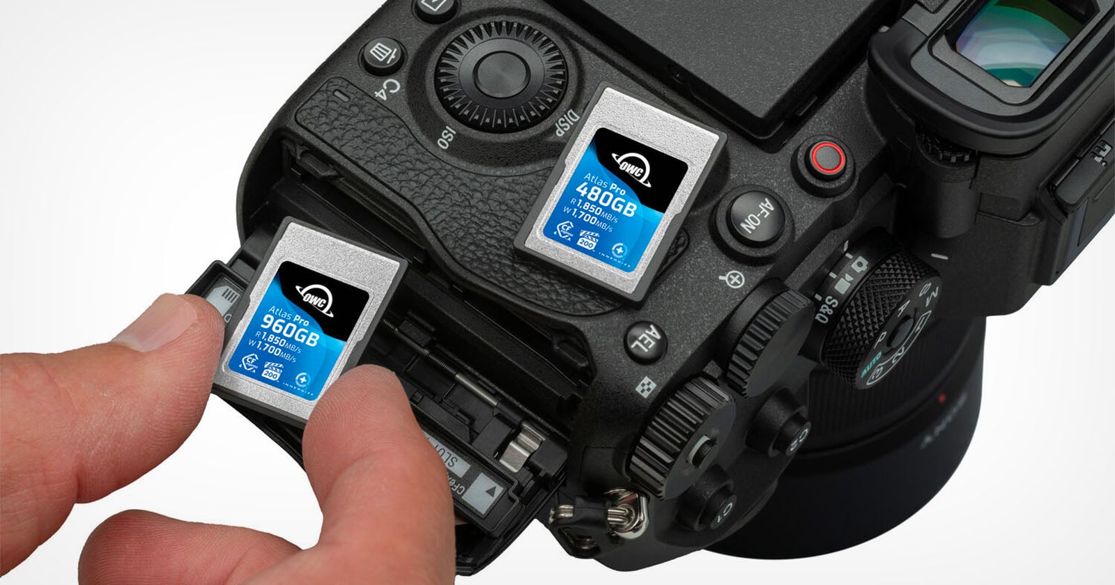 A hand inserts a memory card labeled “960GB” into a camera. Another memory card labeled “480GB” is inserted beside it. The camera shows detailed buttons and controls near the card slots.