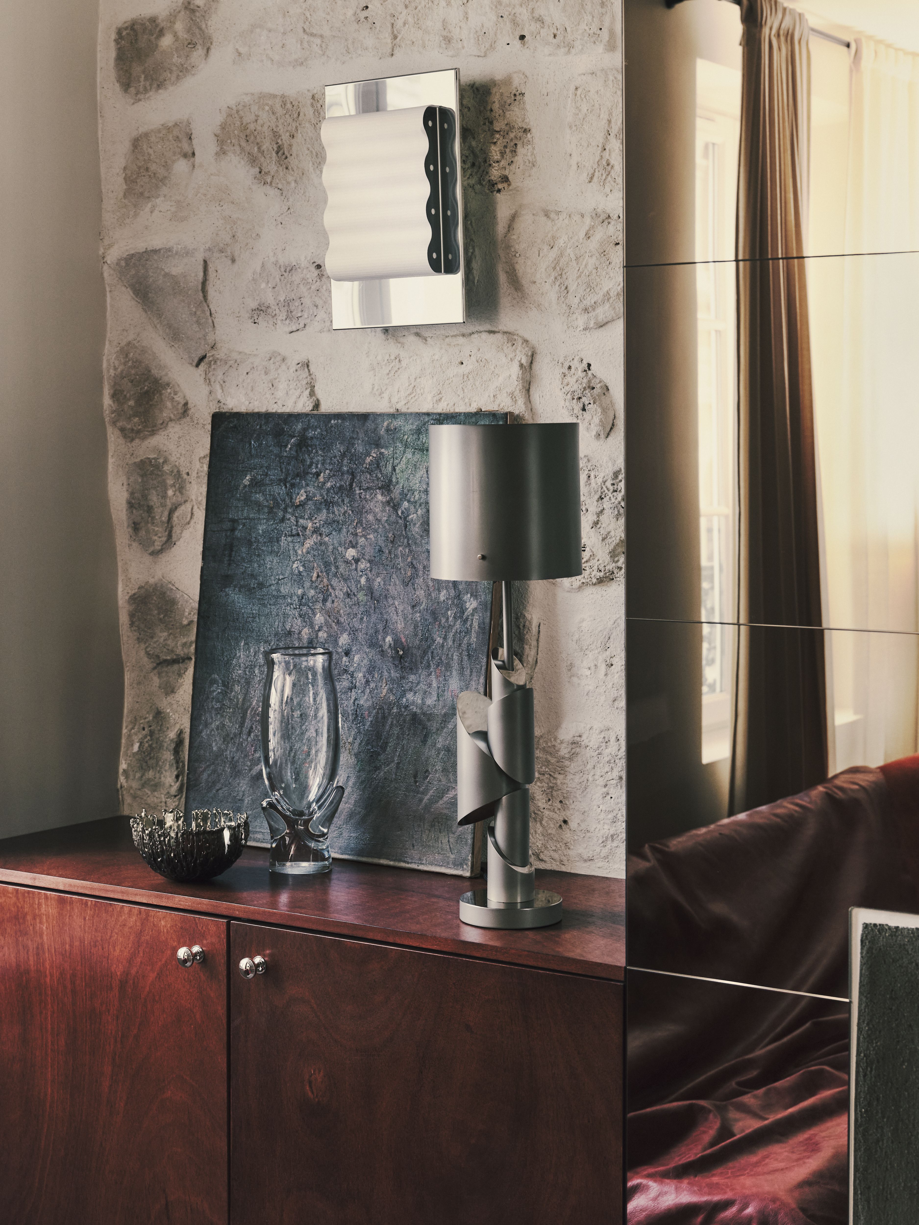 A sleekly designed apartment with tiled white and black checkered floors, chrome surfaces, brick walls, and occasional pops of red, ming green, and butter across linearly cut furniture.