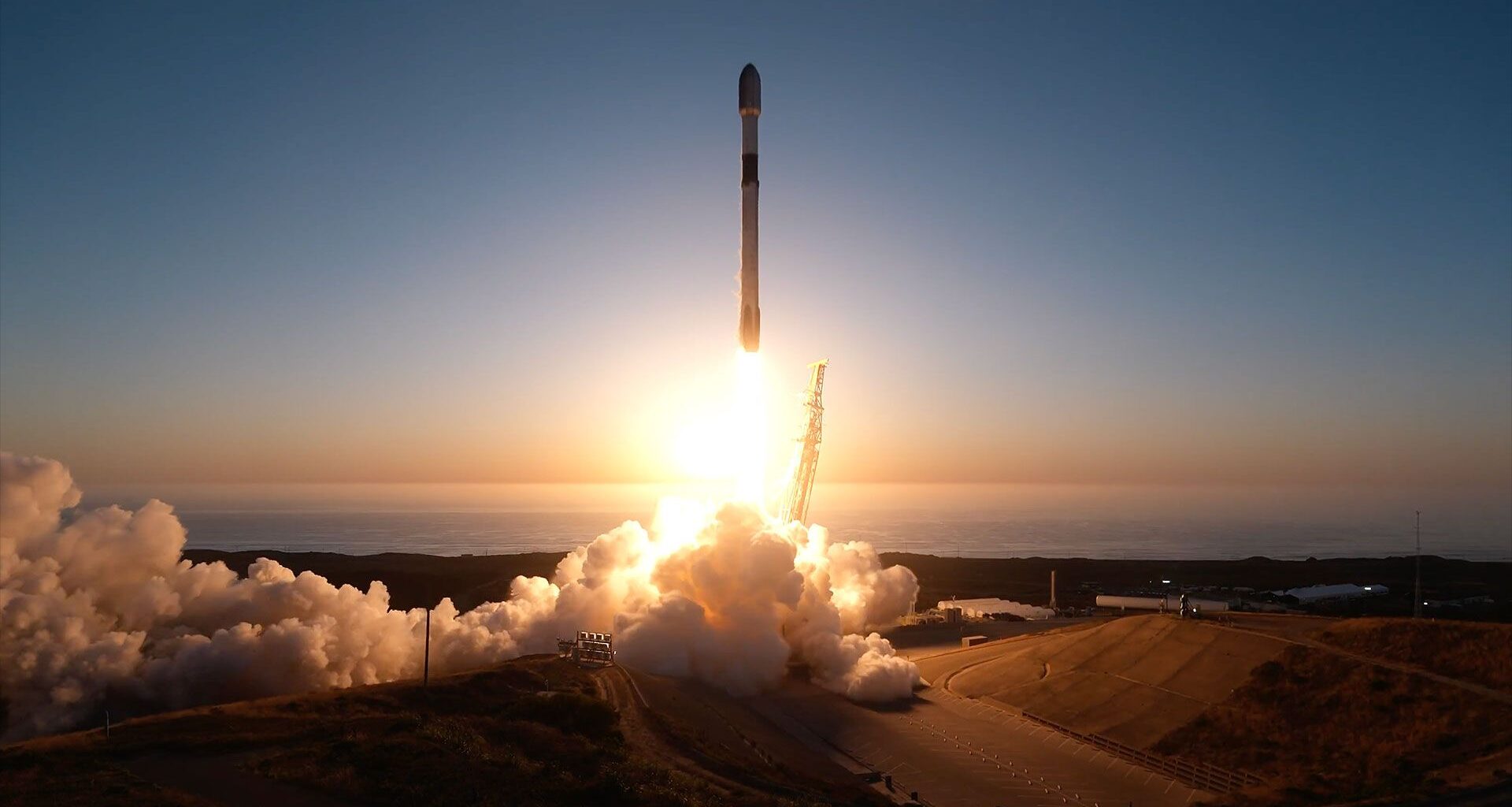 A rocket appears in silhoutte as it lifts off for space backdropped by the setting sun.