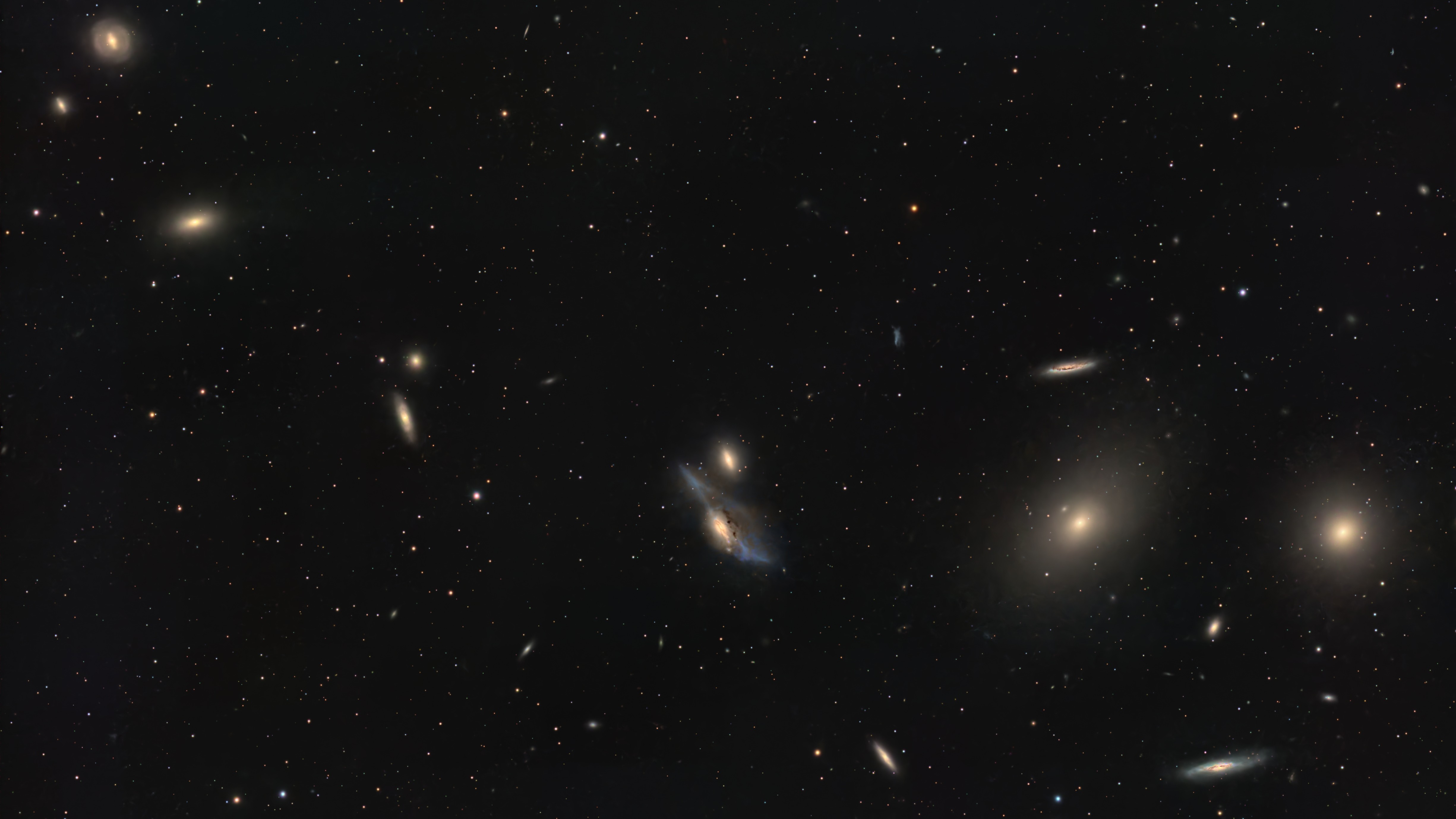 A string of galaxies shines in a deep space photo in a black sky dotted with stars.