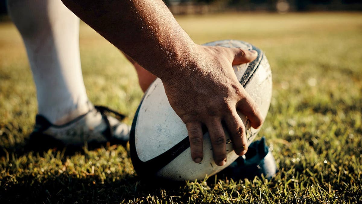 Unrecognizable rugby player preparing to kick ball on field during daytime