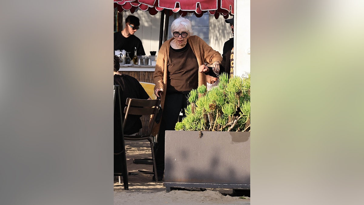 Shirley MacLaine in a brown shirt and cardigan walking out of a Malibu restaurant in April 2026.