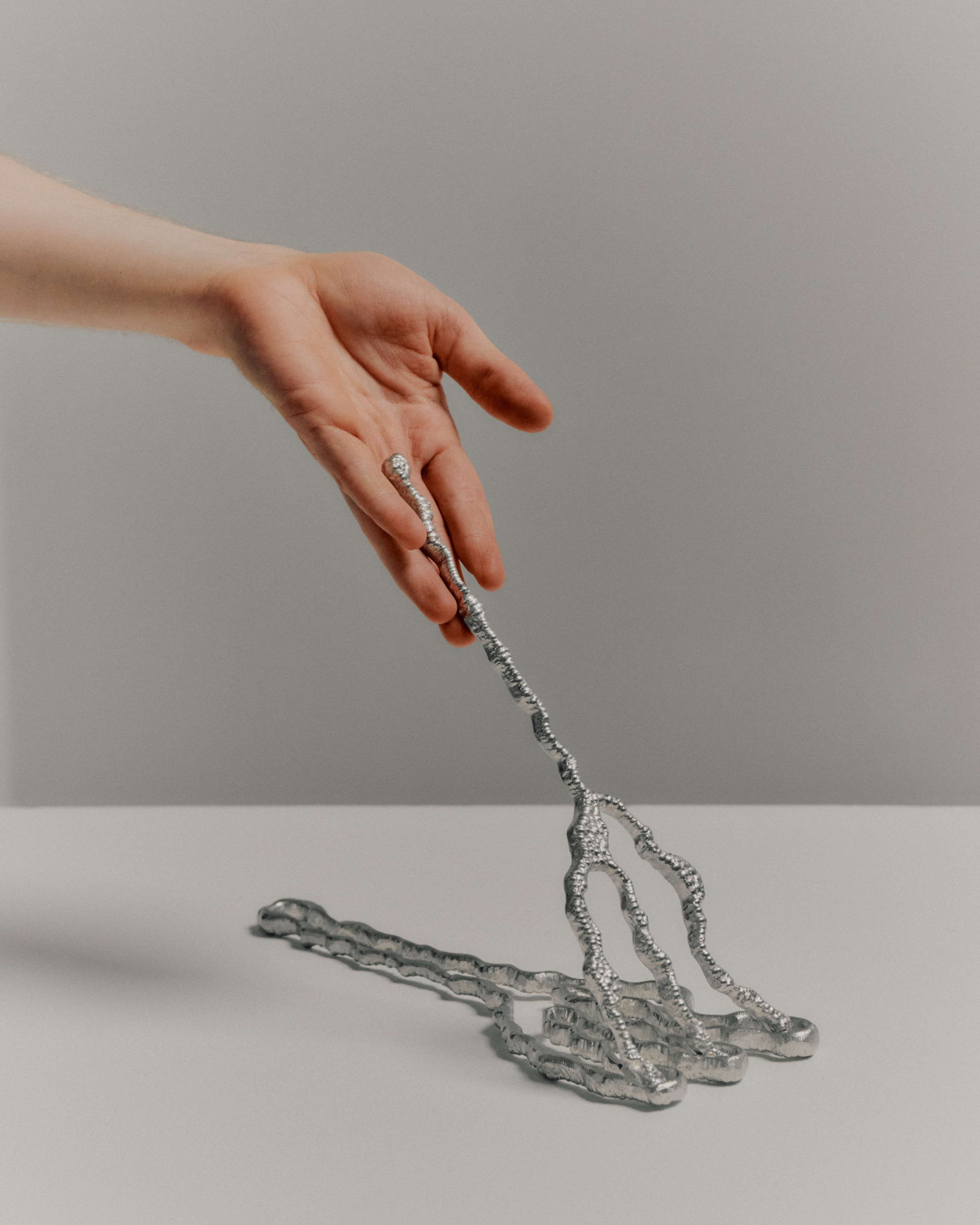 Sculptural forks in textural chrome, held up my a hand in an empty room.