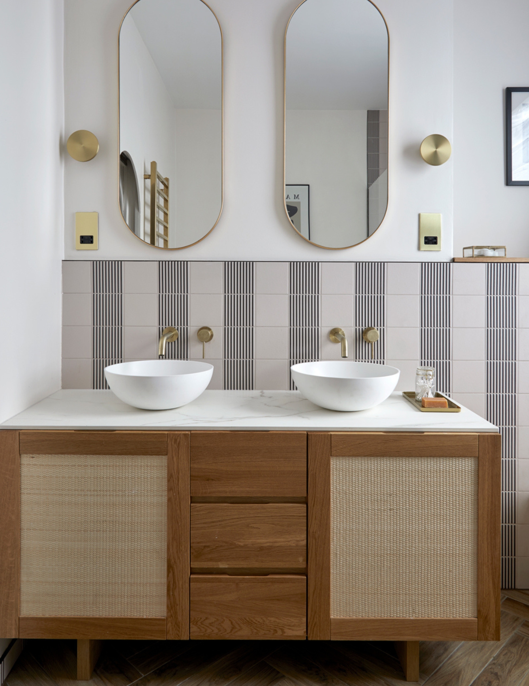 a bathroom with wooden vanity, striped tiles and pill shape bathroom mirrors