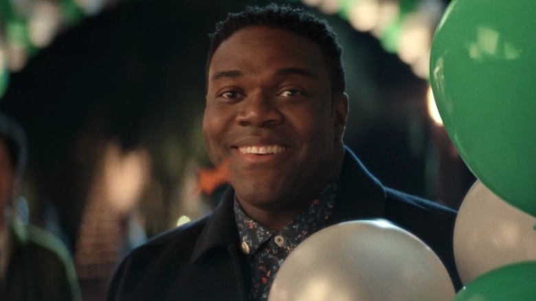 Aniq (Sam Richardson) standing behind balloons and smiling on The Afterparty S1E1