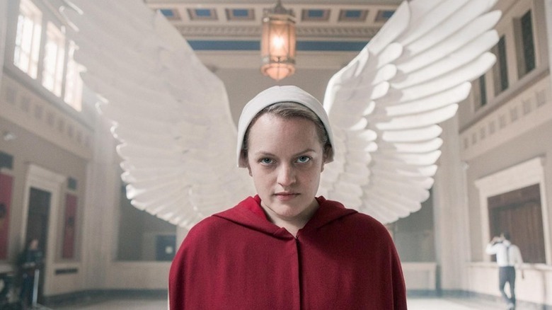 June in red jacket and white hat with angel wings behind her, looking on