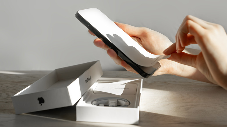 A person removing the paper screen protector covering an iPhone 14 after removing it from the retail box.