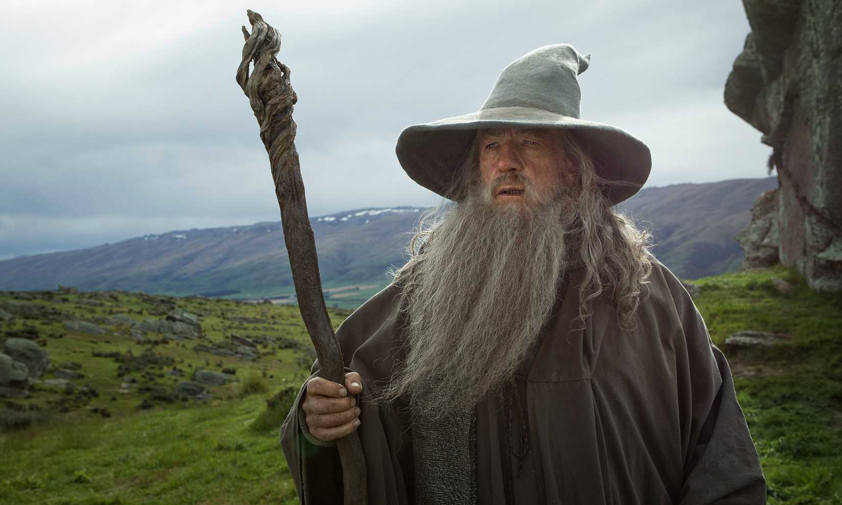 Gandalf the Grey holding his staff with a verdant, hilly field behind him in The Hobbit: An Unexpected Journey