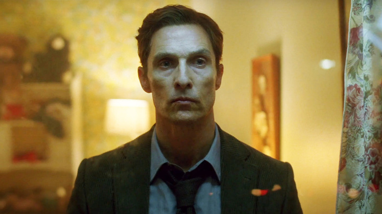Rust Cohle stands in a dimly lit room