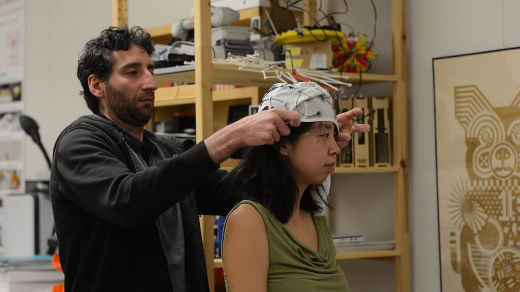 Scientist puts EEG cap on woman in lab setting.