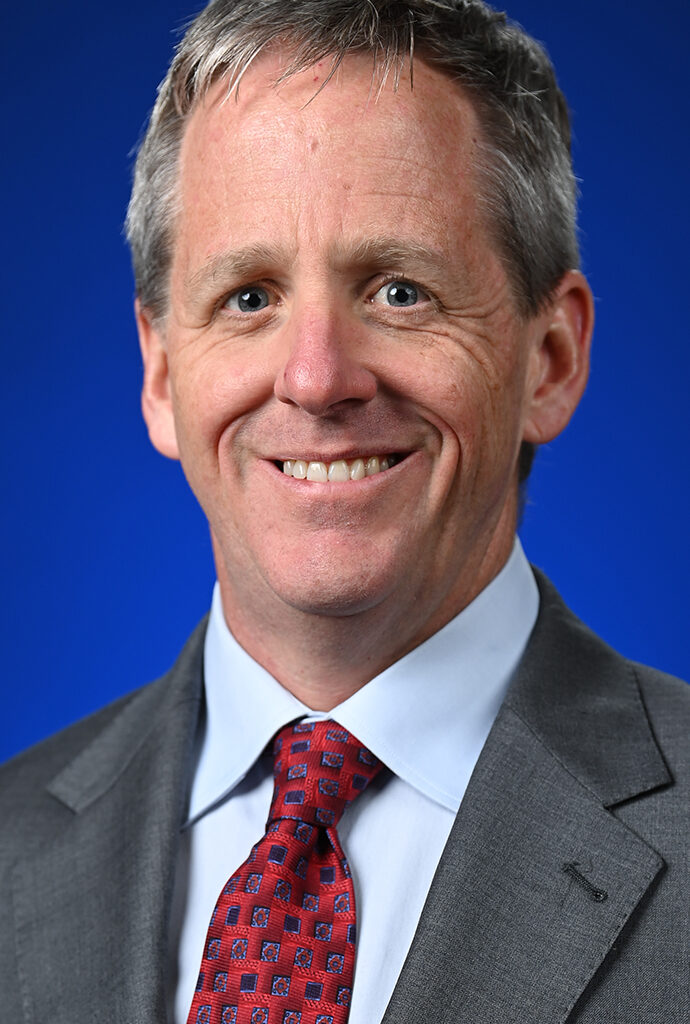 Headshot of a man wearing a gray suit with a red tie.