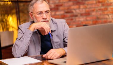 Serious person staring at laptop screen and holding pen.