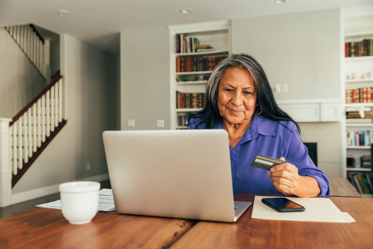 Smiling person holding debit card and typing on laptop.