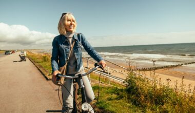 Smiling person riding bicycle by the ocean.