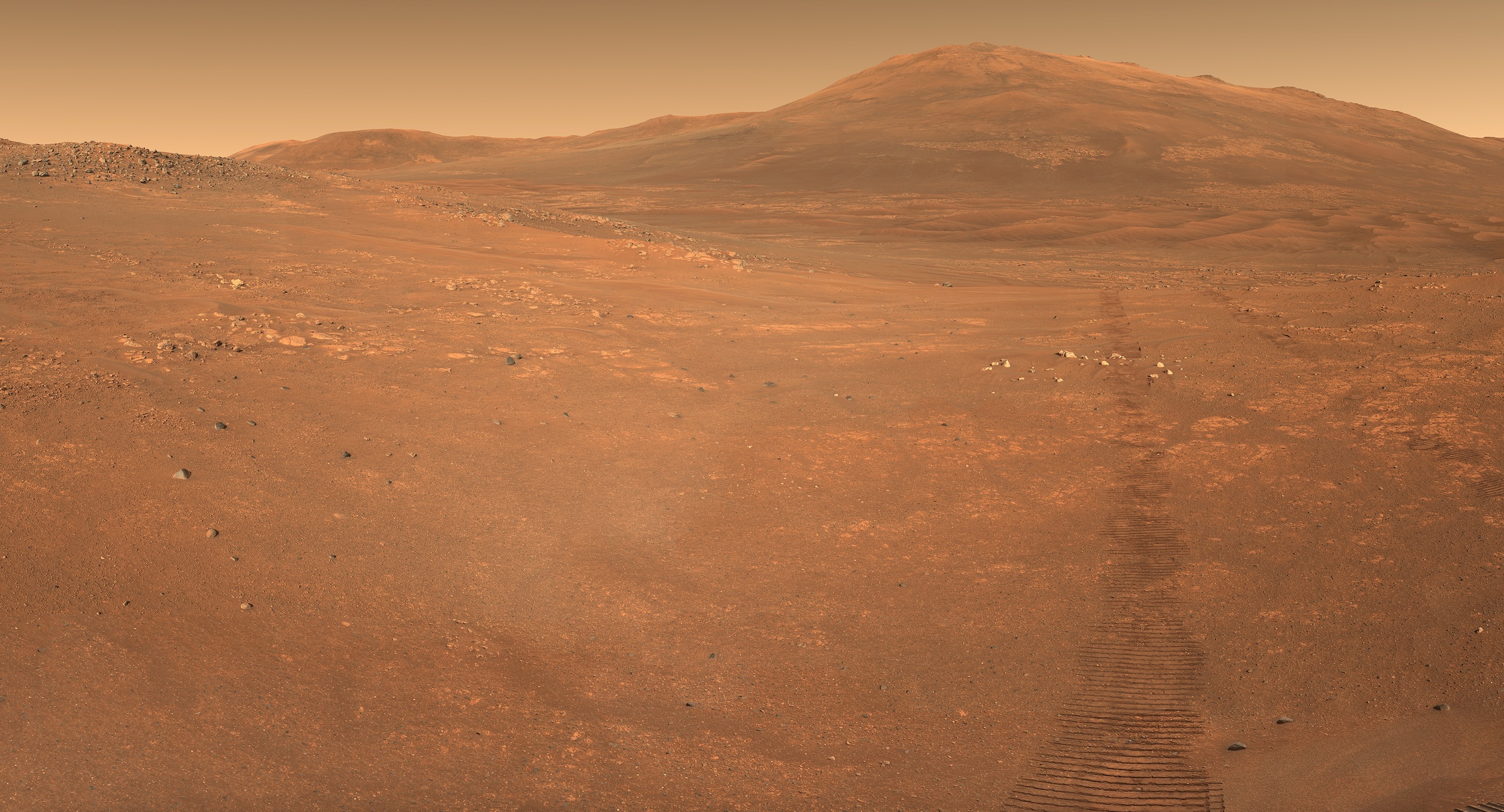 photo of mars taken by a rover, showing a red-dirt desert with a mountain in the background and a line of rover tracks in the foreground