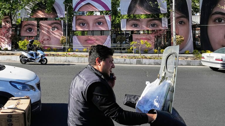 Vehicles drive past banners showing portraits of the school children who were killed during a strike on a school in southern town of Minab