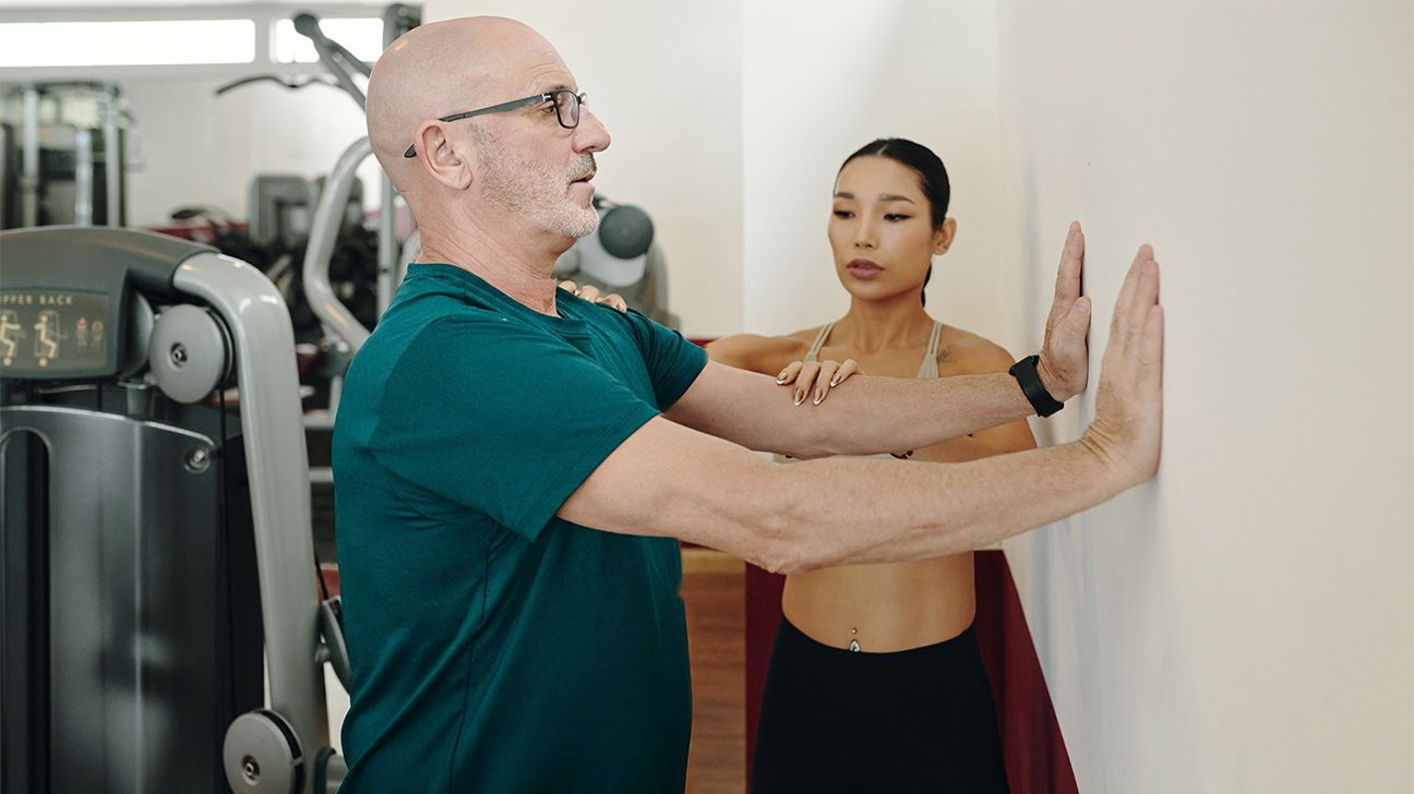 Older male performs a wall push-up with trainer