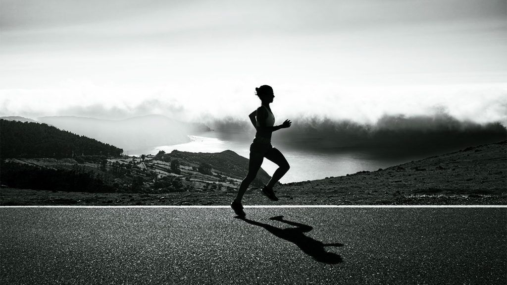 Silhouette of runner on mountain road with dramatic landscape.