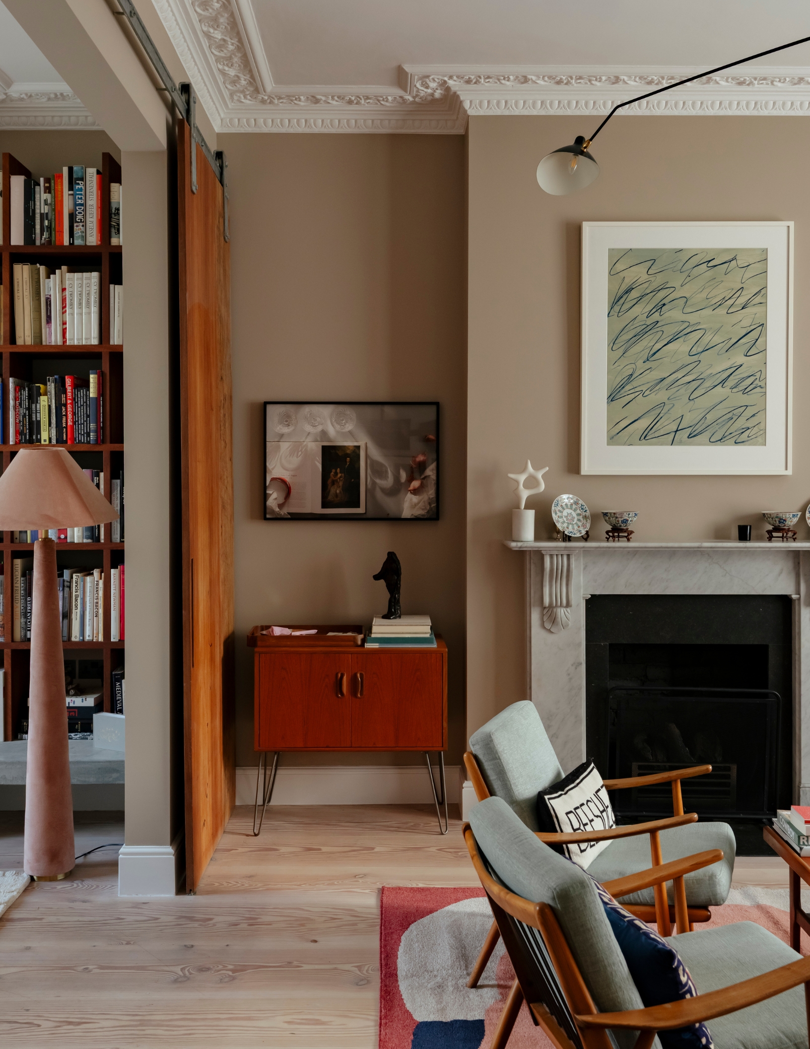 a living room with beige walls, art, and books, surrounding a fireplace