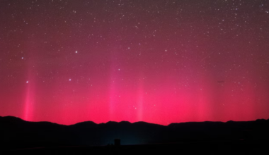 The silhouette of what looks like mountains on the bottom of the screen with bright pink and red lights in the sky above.