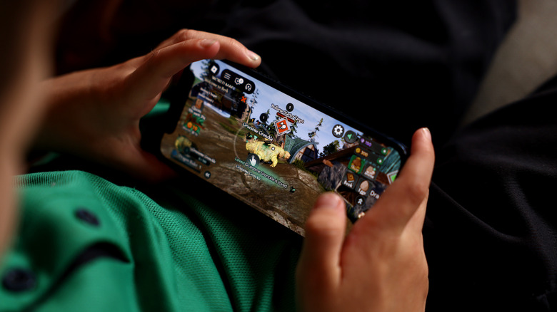 Child in green shirt playing Roblox on an iPhone.