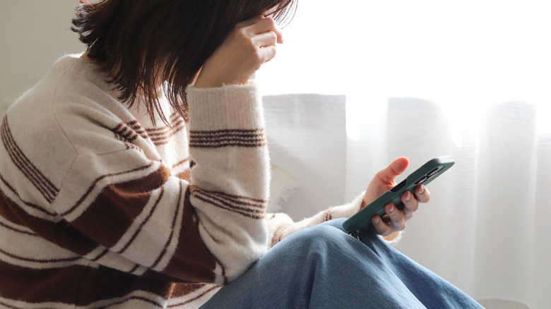 Woman sat on floor using smartphone looking sad.