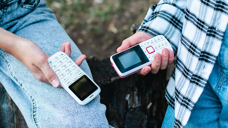 Two people holding numpad mobile phones near each other.