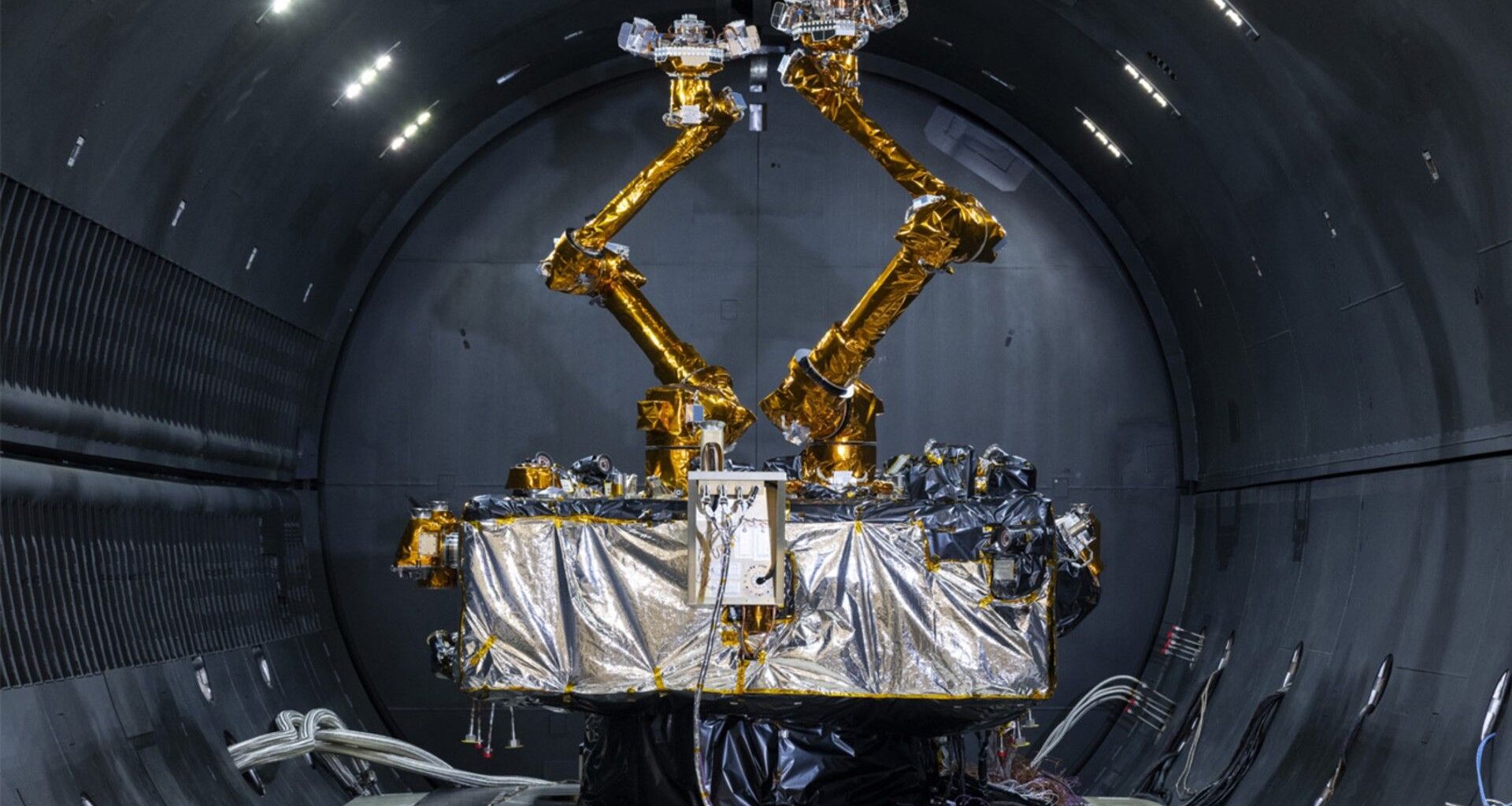 a cube-shaped satellite with two multi-jointed arms inside a cleanroom