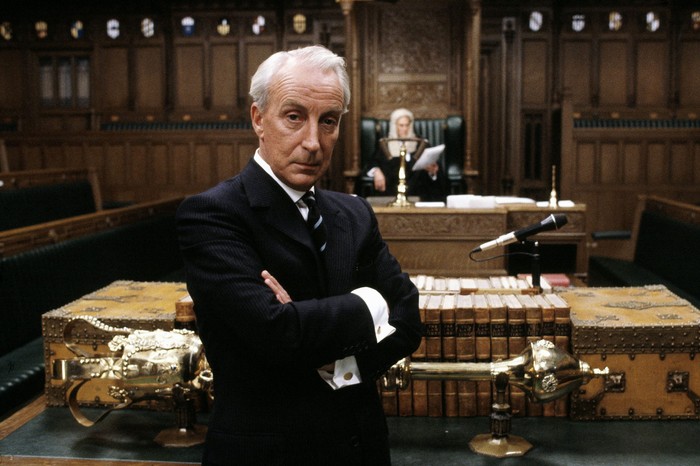 Ian Richardson as Frances Urquhart in House of Cards, wearing a suit, with his arms folded.