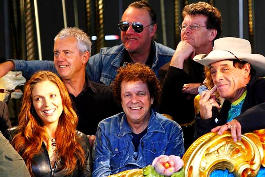 A group of men, including one in a white cowboy hat, and one woman sit in a close group.