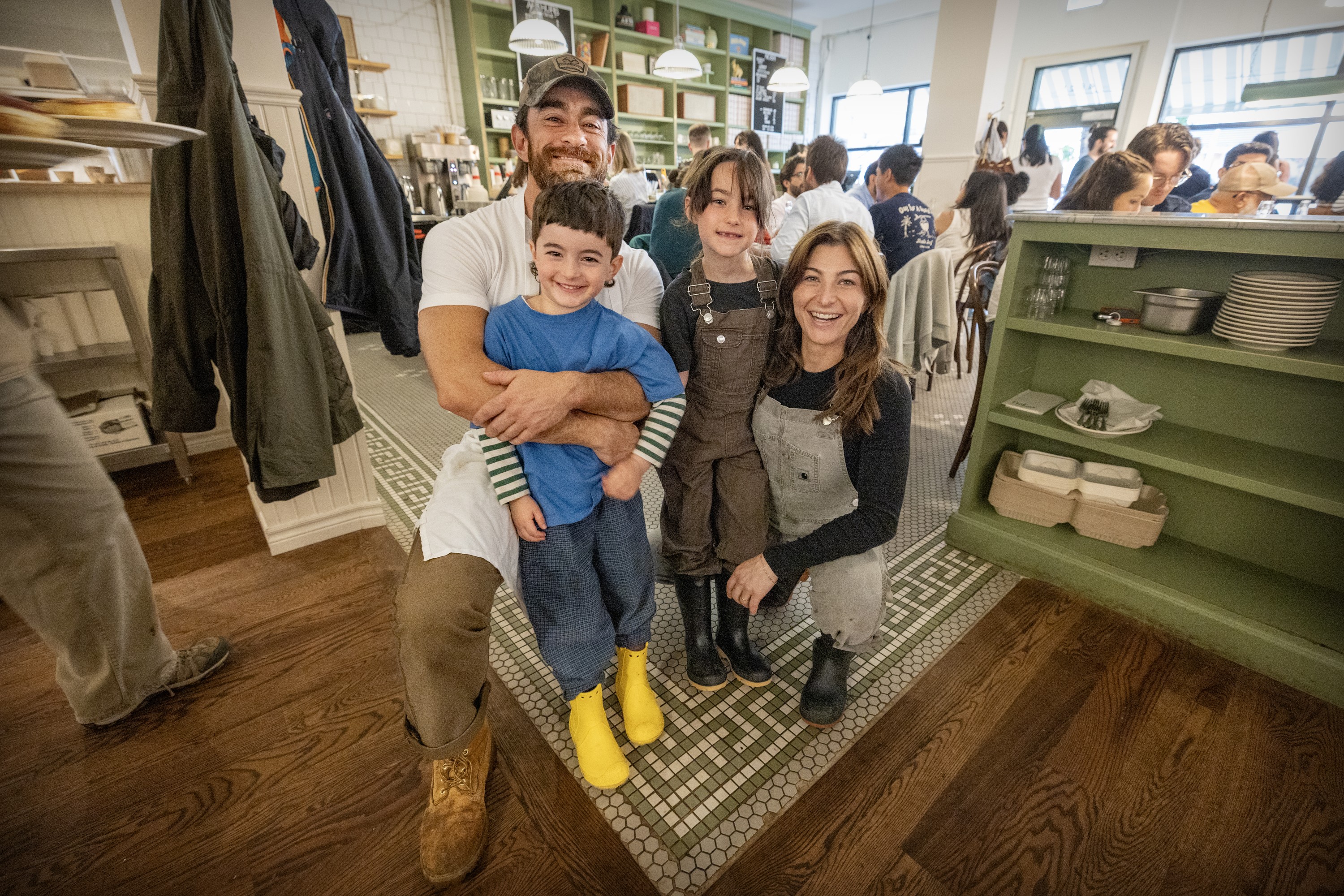 A man and woman hug two young children while looking at the camera in a busy restaurant.