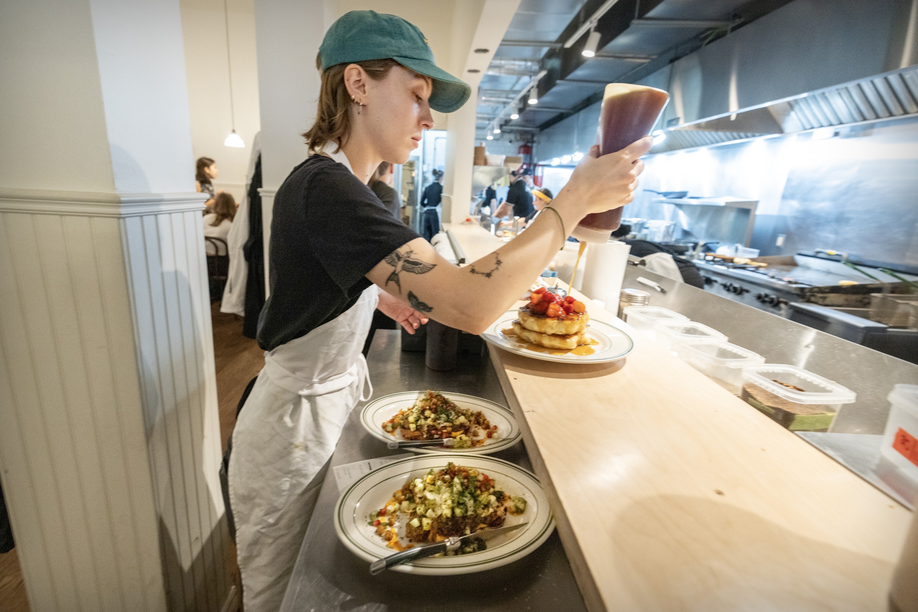 A woman working in a restaurant pours syrup on pancakes.