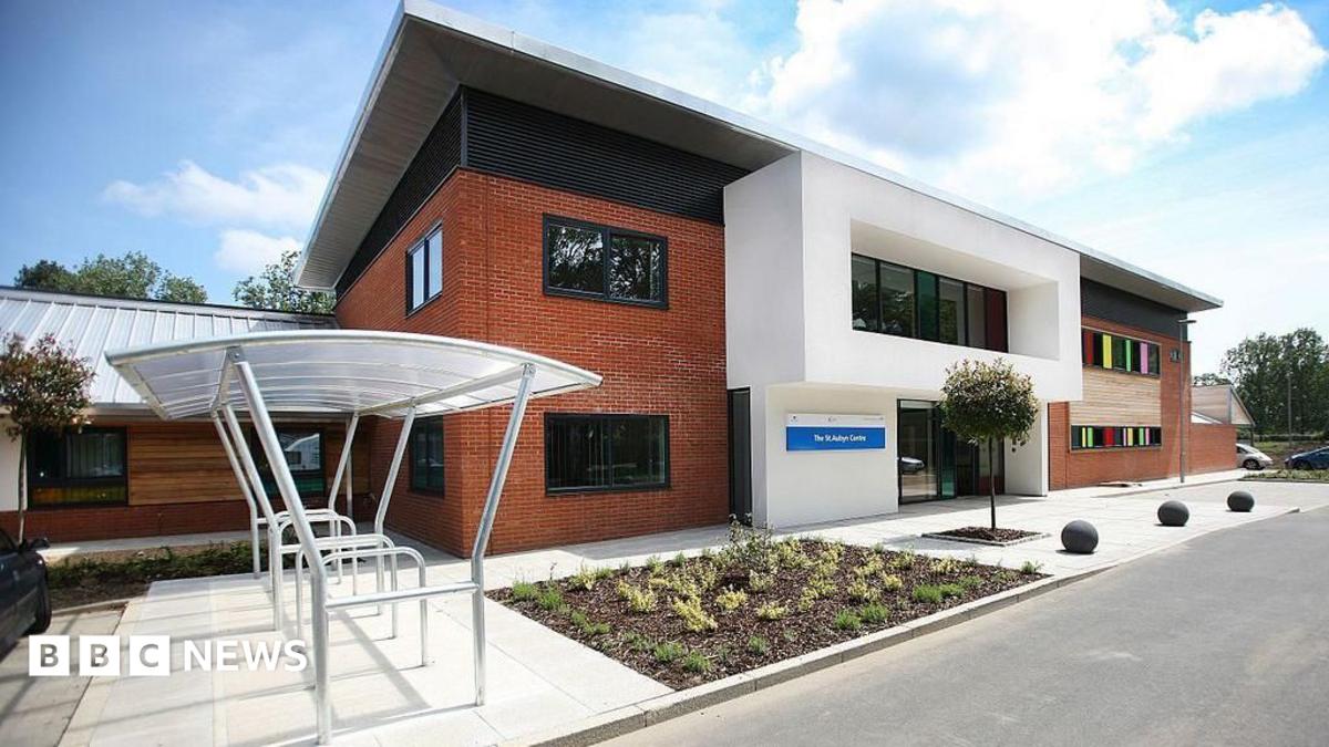 The front of the St Aubyn Centre. It is a red brick building with a cycle rack outside. There are rainbow-coloured windows to the side and it has a few plants in a flowerbed at the front.