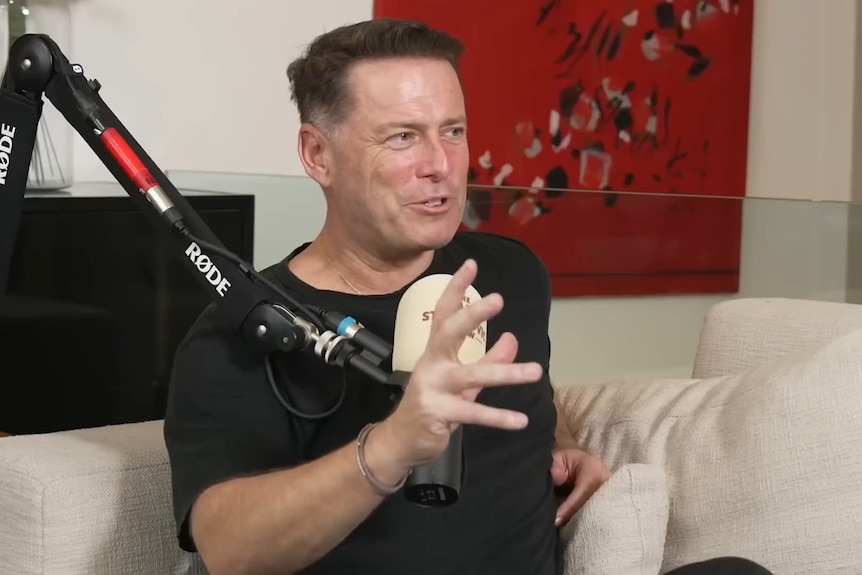 A man in black sits behind a microphone.