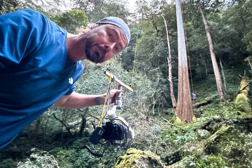 A man has a camera on a rope coming off a tree.
