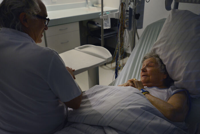 A nurse compassionately talks with an elderly patient lying in a hospital bed, providing comfort and care.