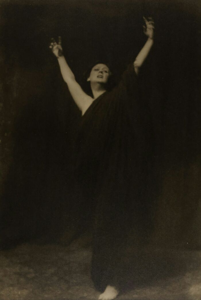 A dramatic black and white photo of a woman in a dark dress with arms raised, reflecting unexplained events nurses see in patients.